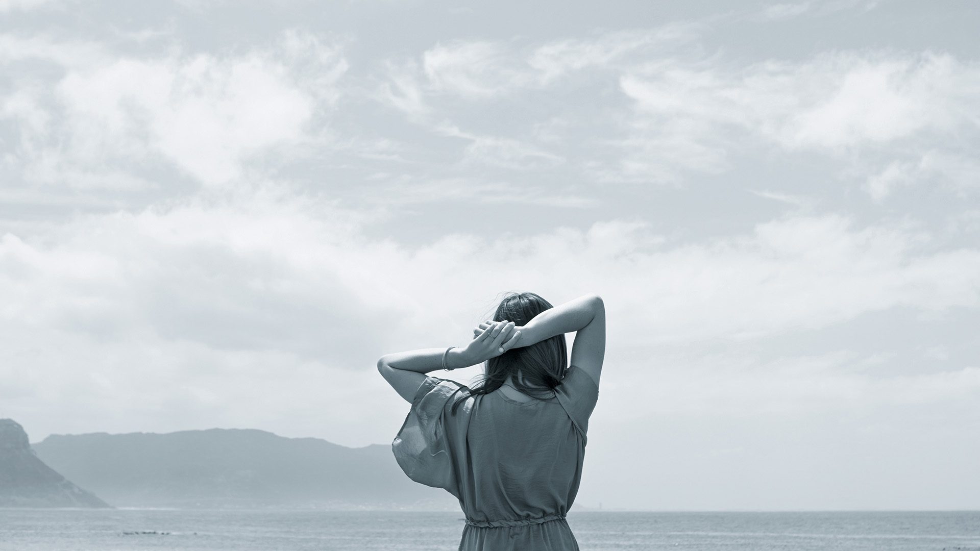 Rearview shot of the head and sholders of a woman looking out at the ocean with sky above